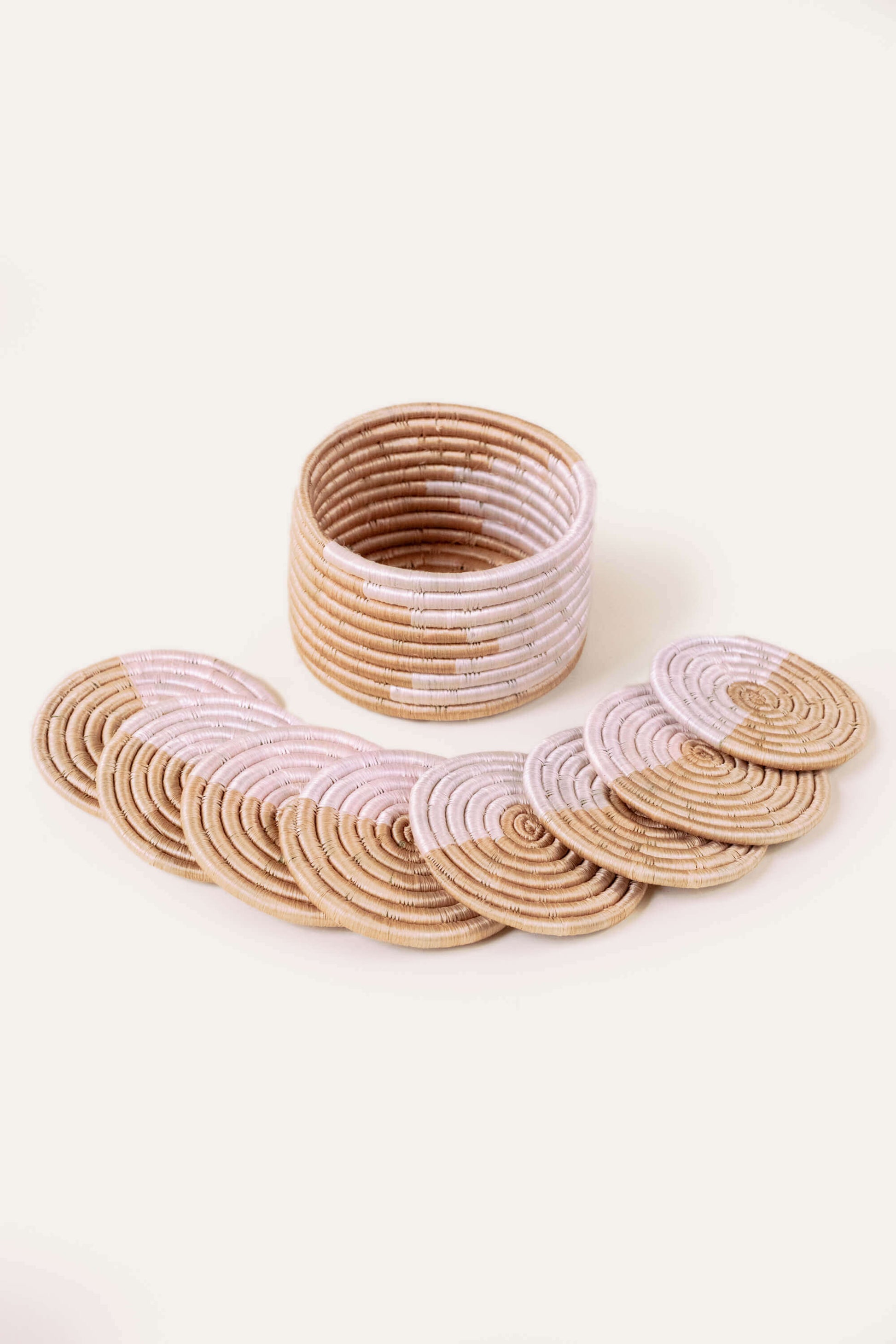 A set of 8 blush and natural colored coasters with a woven design, displayed alongside a small trinket basket. ethically made. fair trade. 