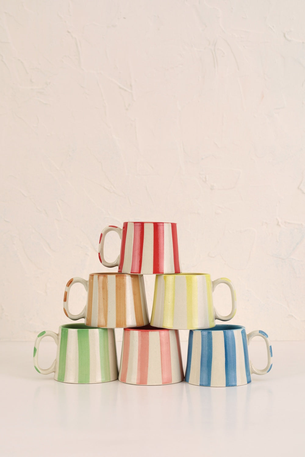 Stack of colorful striped mugs on a light background