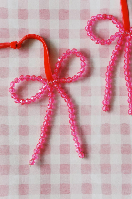 Pink beaded bow Christmas ornaments on a pink and white checkered background - by wallflower