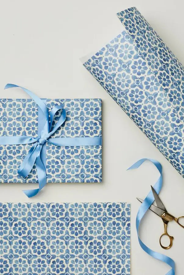 Blue floral tile patterned gift wrap with a ribbon and scissors on a white background