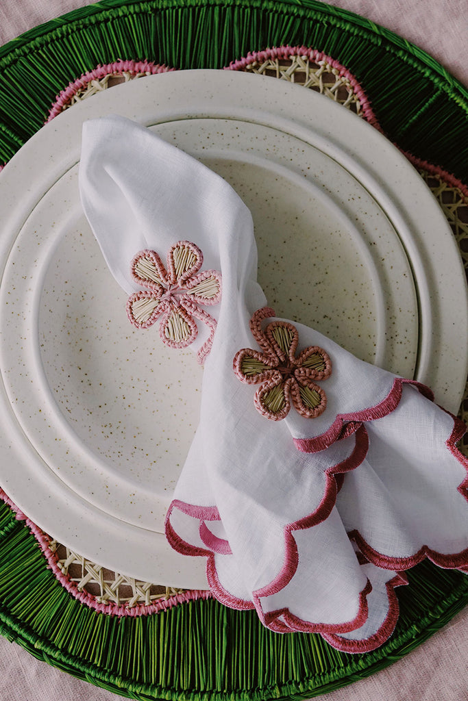 green and pink place setting with woven placemat and flower napkin rings, and pink scalloped napkins from wallflower shop