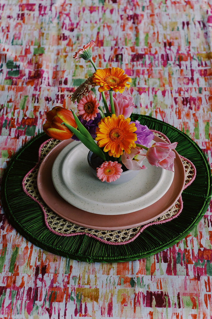 bright maximalist place setting with green palm placemat and orange gerbera daisies