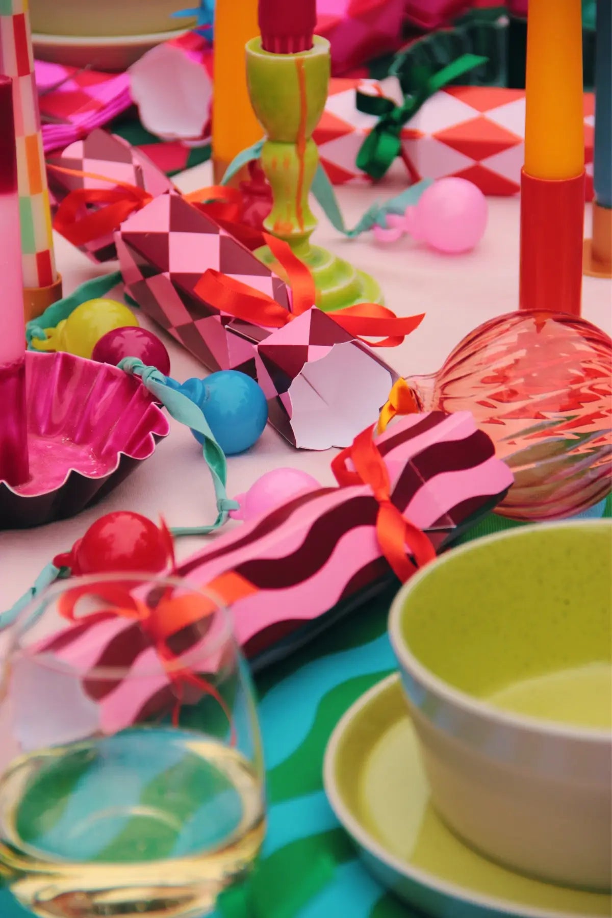 Colorful party decorations and tableware on a table with pink + red Christmas crackers