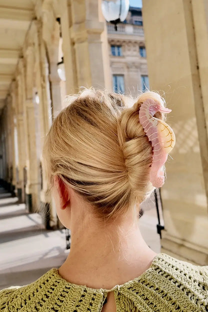 Person with a stylish hair bun wearing a pink sea horse claw clip hair accessory 