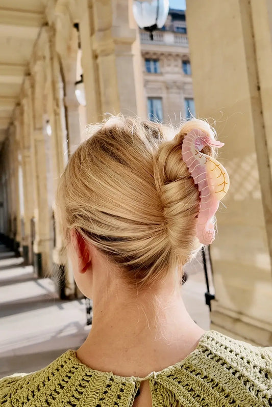 Person with a stylish hair bun wearing a pink sea horse claw clip hair accessory 