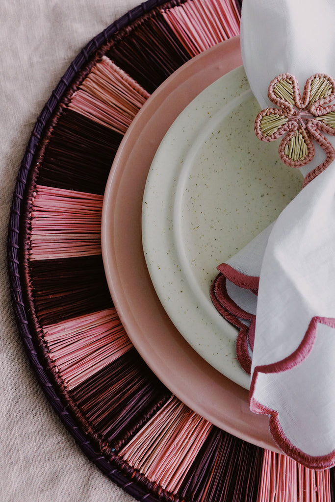 closeup of pink place setting with woven placemats and floral napkin ring