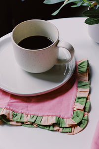 cup of coffee on white table with pink and green napkins by wallflower shop